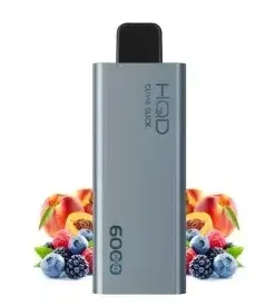 A sleek silver HQD Slick vaping device artfully rests among colorful peaches, blueberries, and raspberries, offering a delightful taste. Get the HQD Slick Bundle of 3 pcs for up to 6000 puffs each.