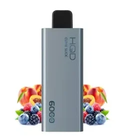 A Bundle 3 pcs HQD Slick 6000 puffs vape device, in a sleek silver design, is positioned in front of a delightful bundle of fruits including berries, peaches, and other mixed varieties.