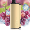 A gold-colored vape device from the "BUNDLE 3 PCS - ALIBARBAR INGOT 9000" collection stands upright in front of a background featuring grapes, ice cubes, and grape leaves.